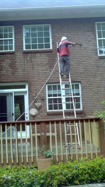 Zelaya Jr. technician on a ladder pressure washing the side of a two story home.